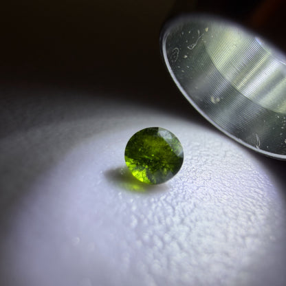 Green gemstone under a magnifying glass on a white surface