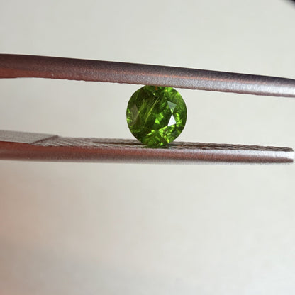 Green gemstone held between tweezers against a neutral background