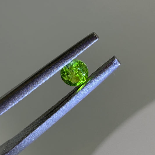 Green gemstone held between tweezers against a neutral background