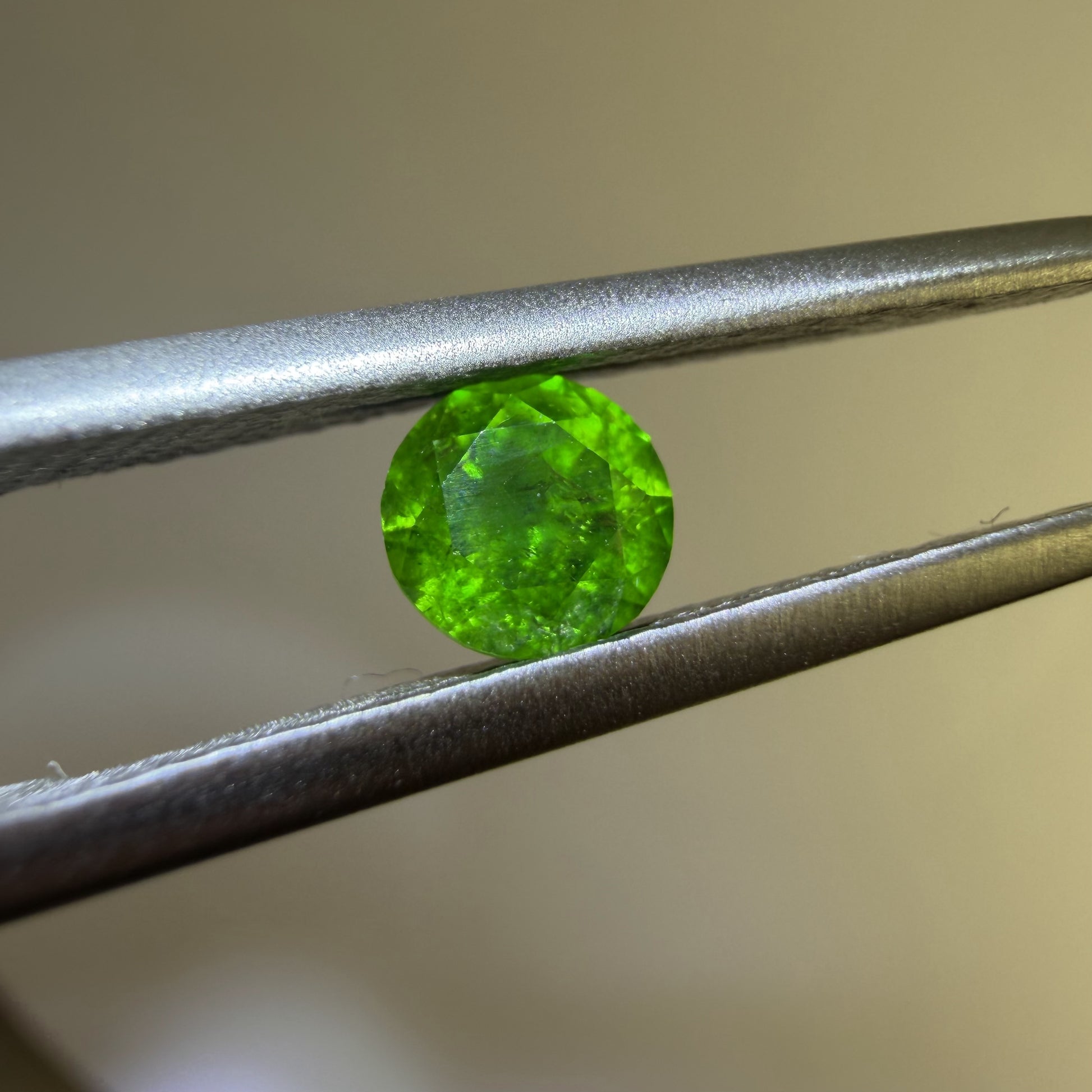 Green gemstone held between tweezers against a neutral background