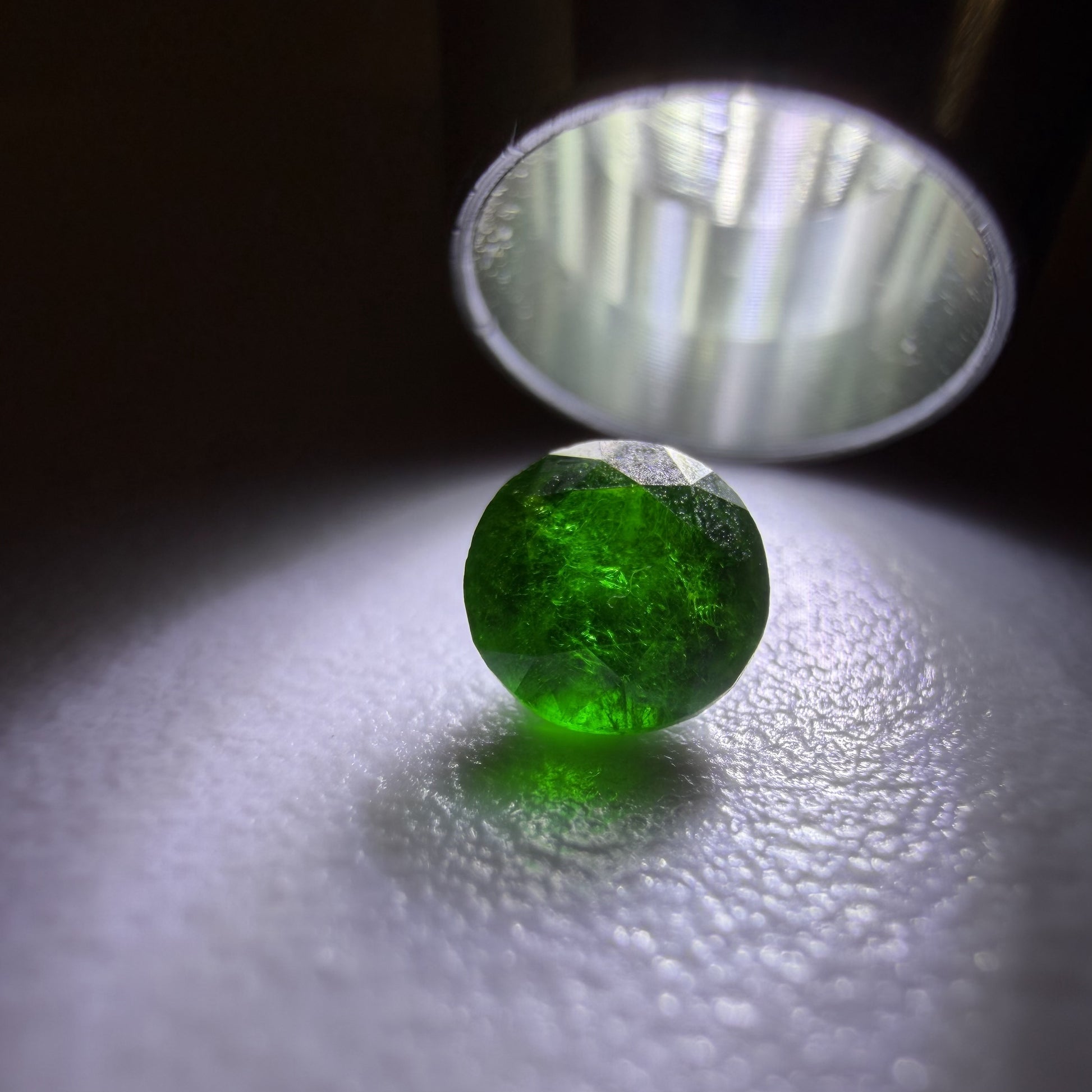 Green gemstone under a lamp on a reflective surface