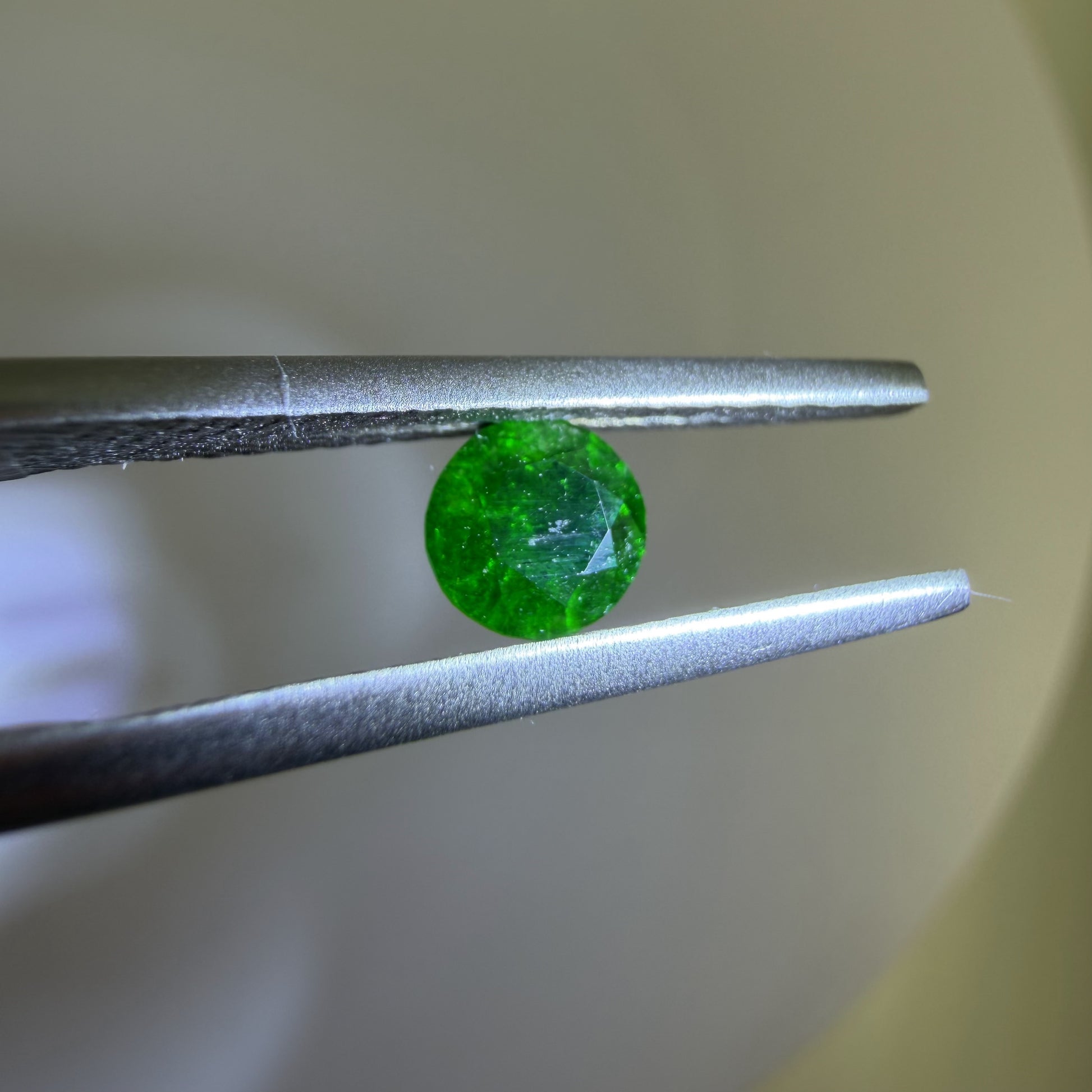 Green gemstone held between tweezers against a neutral background