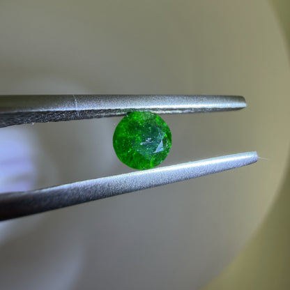 Green gemstone held between tweezers against a neutral background