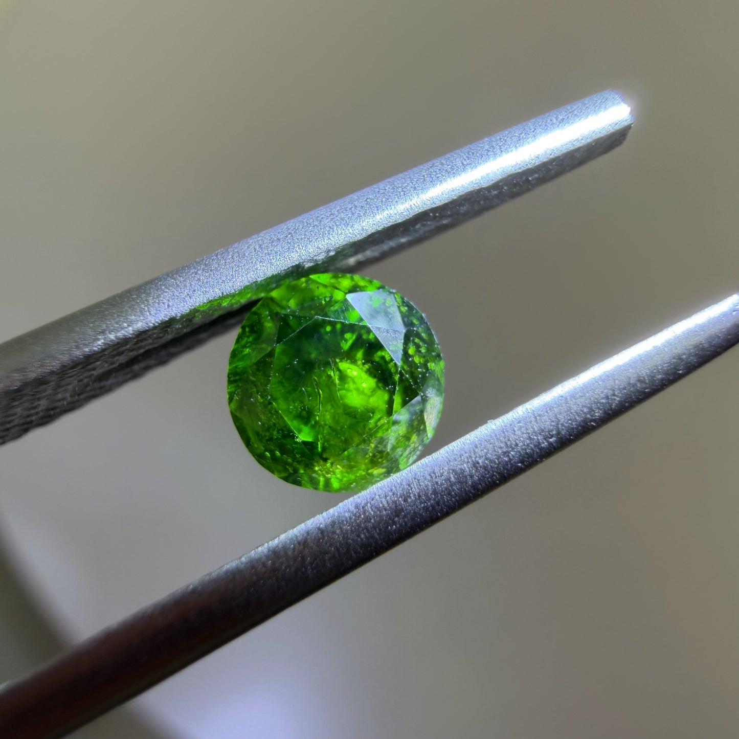 Green gemstone held between tweezers against a neutral background