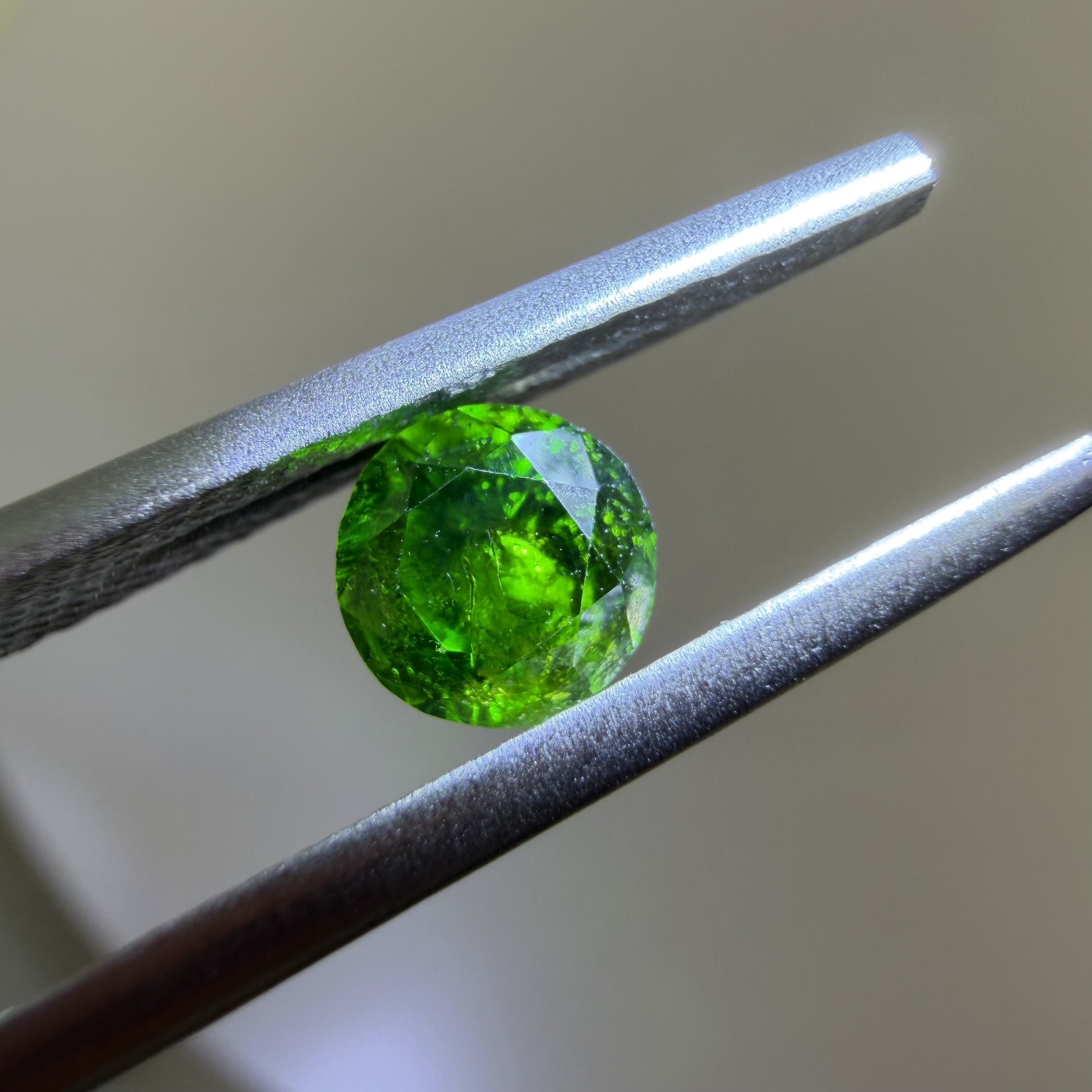 Green gemstone held between tweezers against a neutral background
