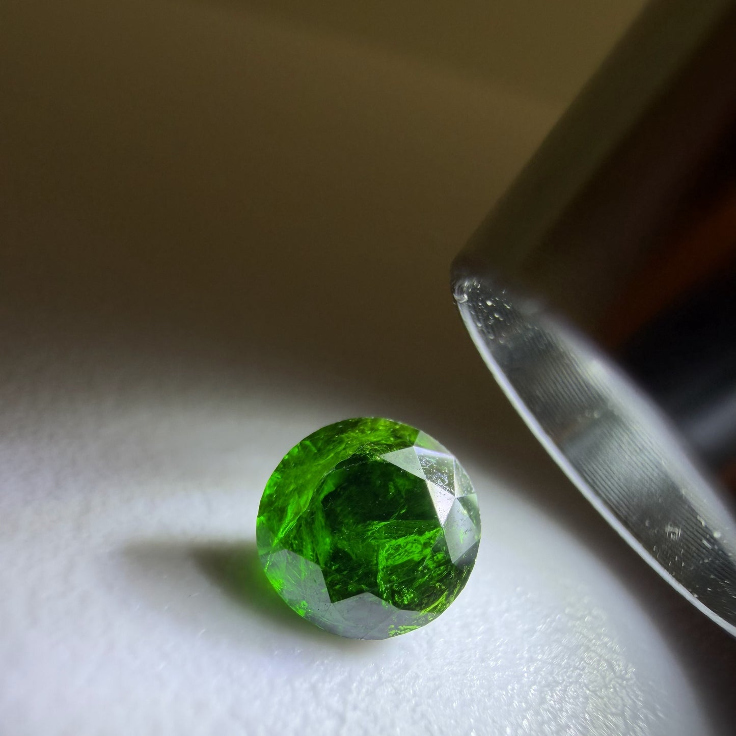 Green gemstone on a white surface with a magnifying glass
