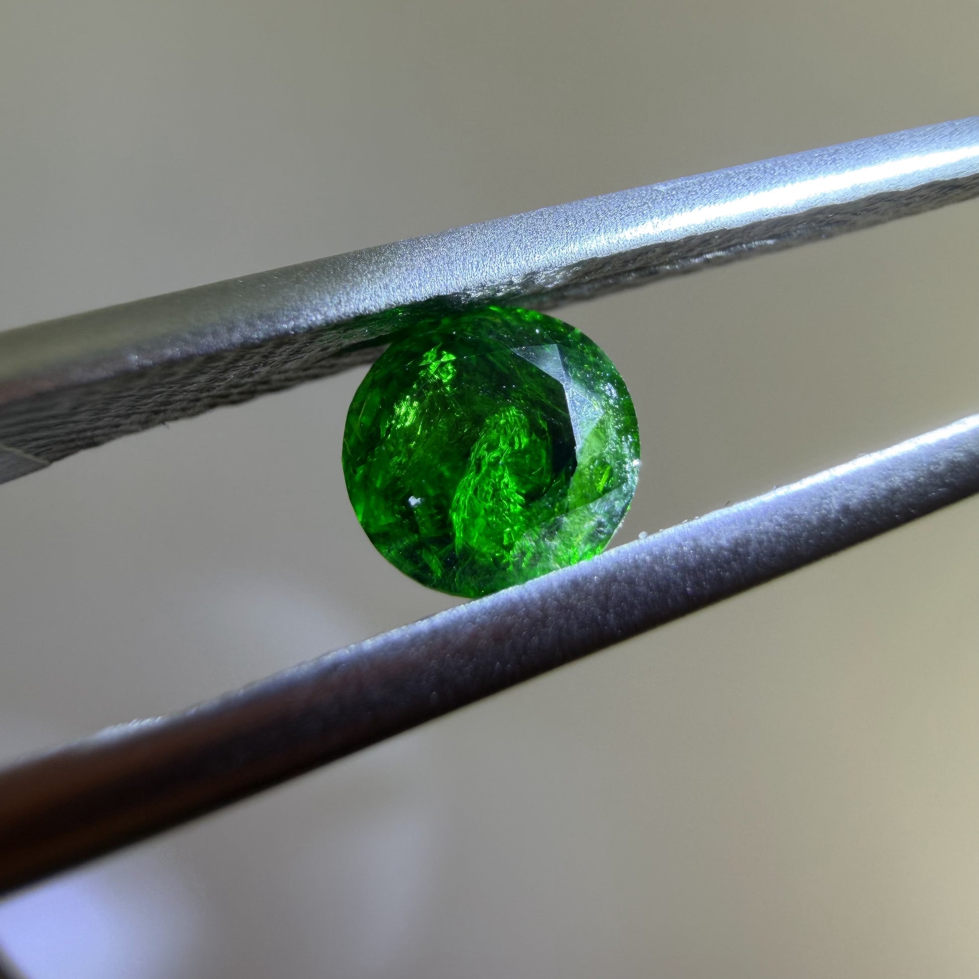 Green gemstone held between tweezers against a neutral background