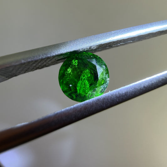 Green gemstone held between tweezers against a neutral background