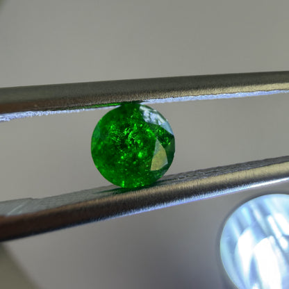 Green gemstone held by tweezers with a light gray background