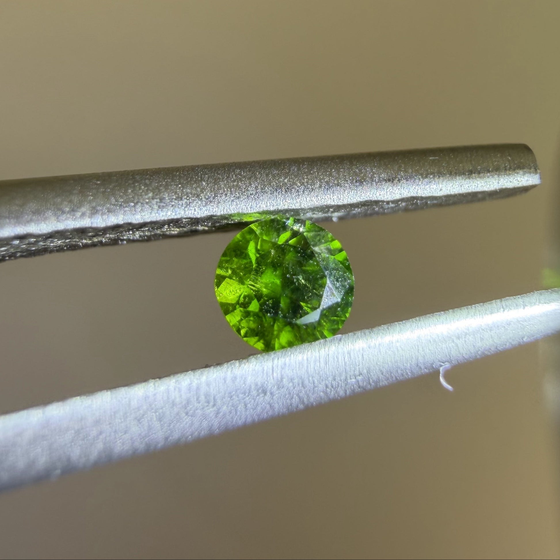 Green gemstone held between tweezers against a neutral background