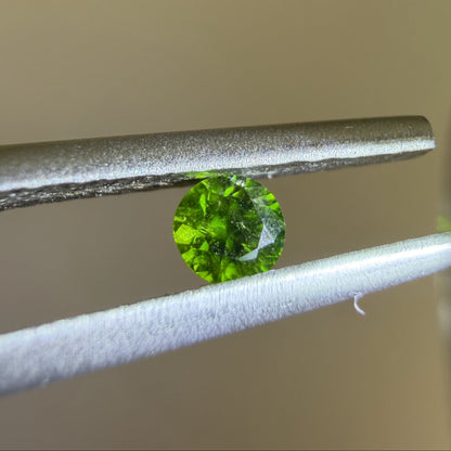 Green gemstone held between tweezers against a neutral background