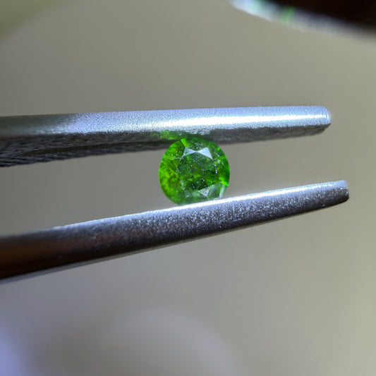 Green gemstone held between tweezers against a neutral background