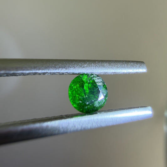 Green gemstone held between tweezers against a neutral background
