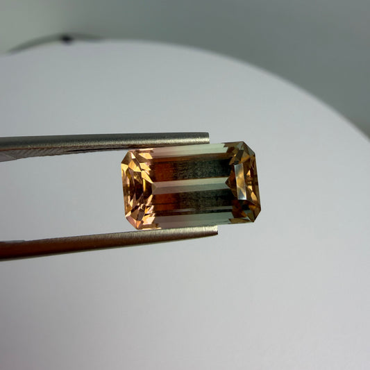 Rectangular cut gemstone held by tweezers on a white background