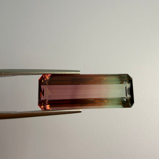 Rectangular gemstone held by tweezers on a light gray background