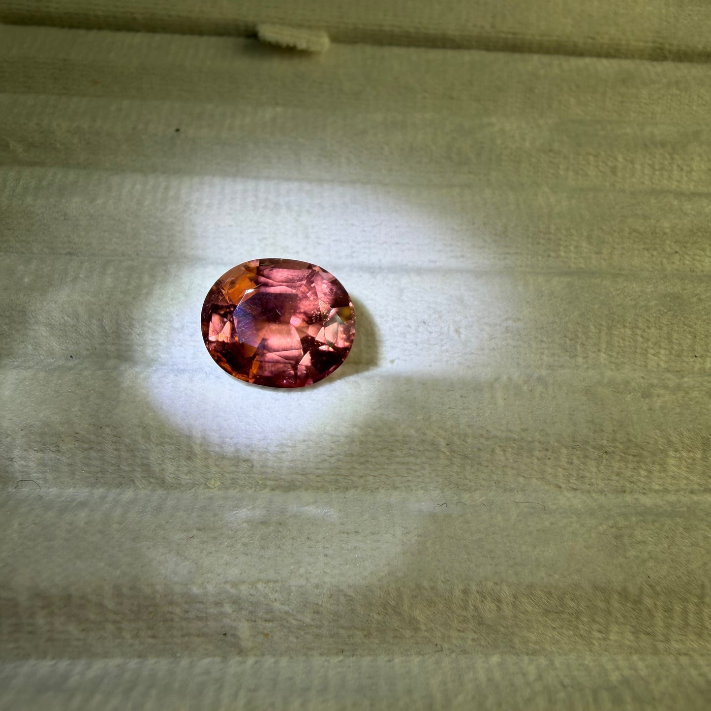 Round pinkish-red gemstone on a textured beige surface