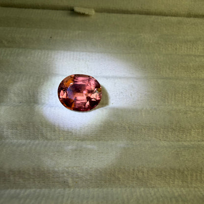 Round pinkish-red gemstone on a textured beige surface
