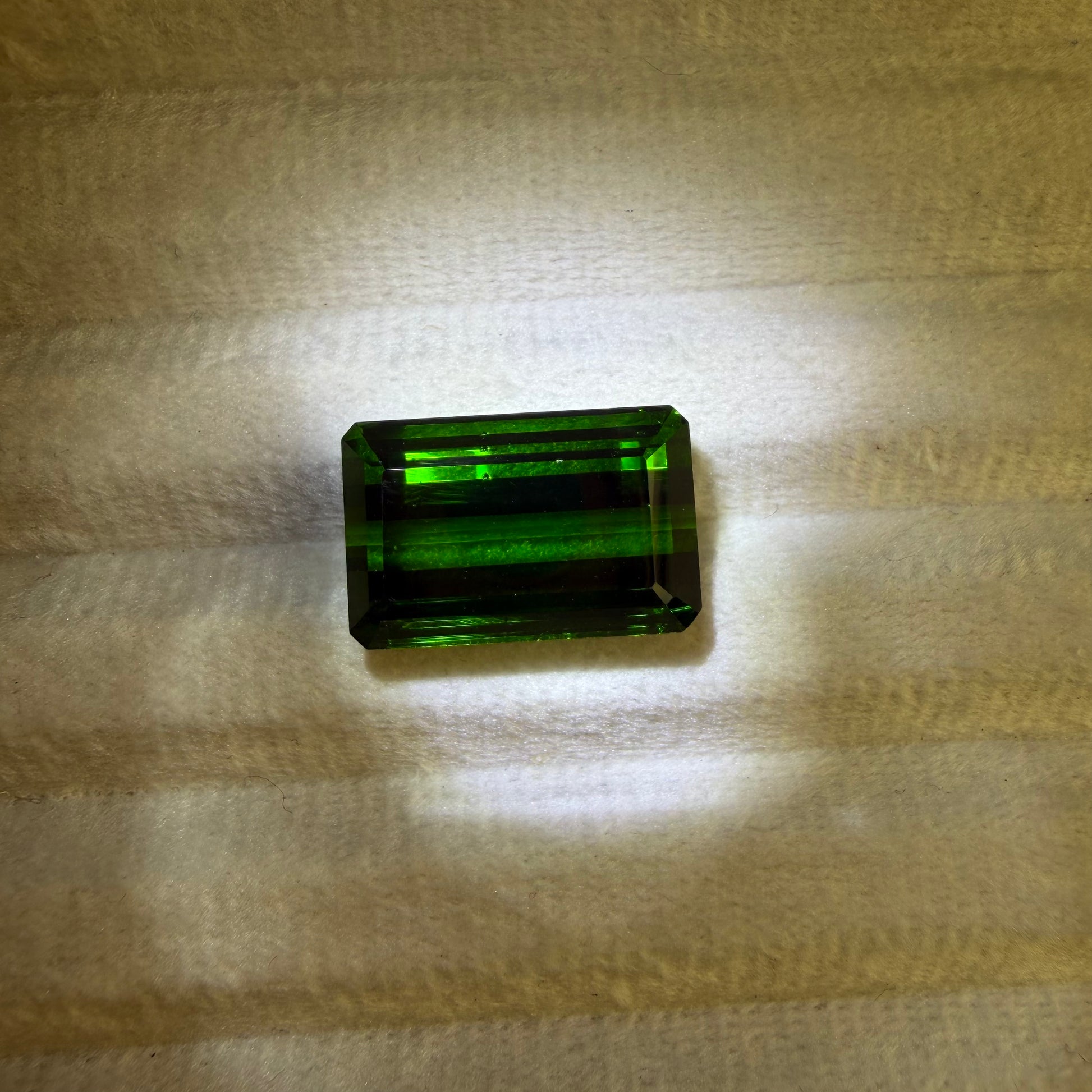 Rectangular green gemstone on a textured beige surface