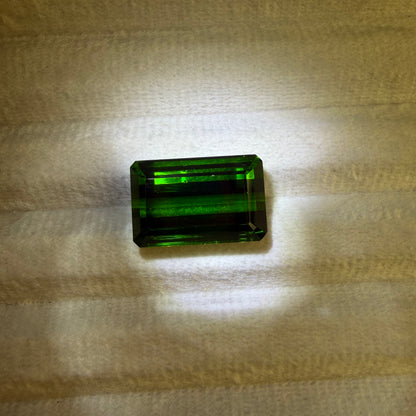 Rectangular green gemstone on a textured beige surface