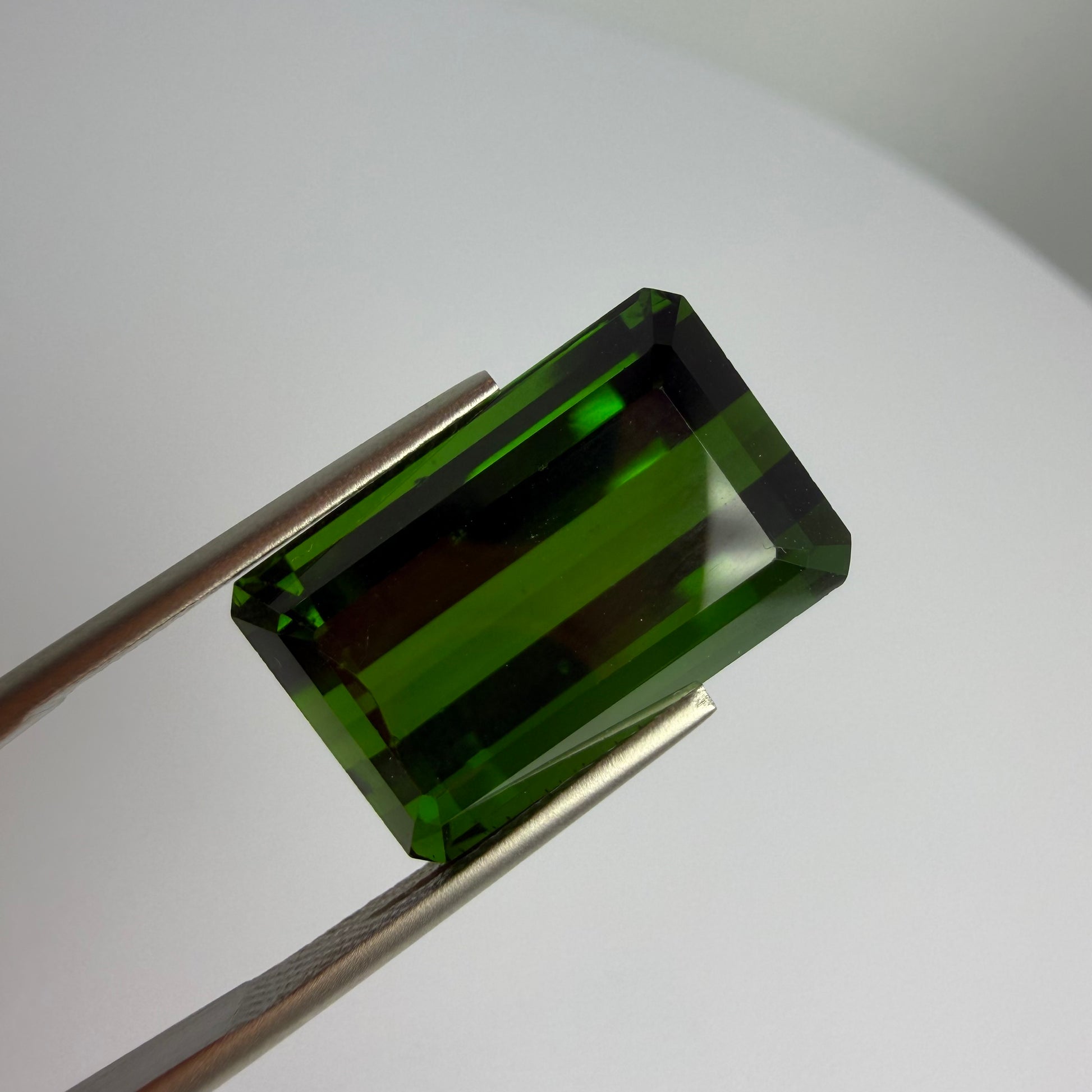 Green gemstone held by tweezers on a white background