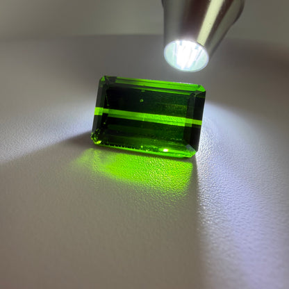 Rectangular green gemstone under a light source on a white surface