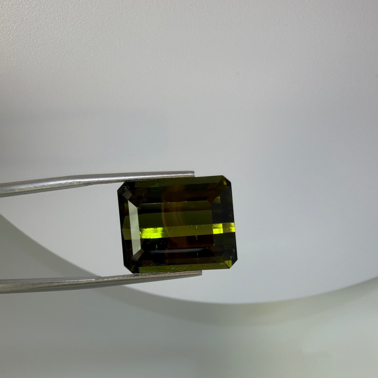 Green gemstone held by tweezers on a white background