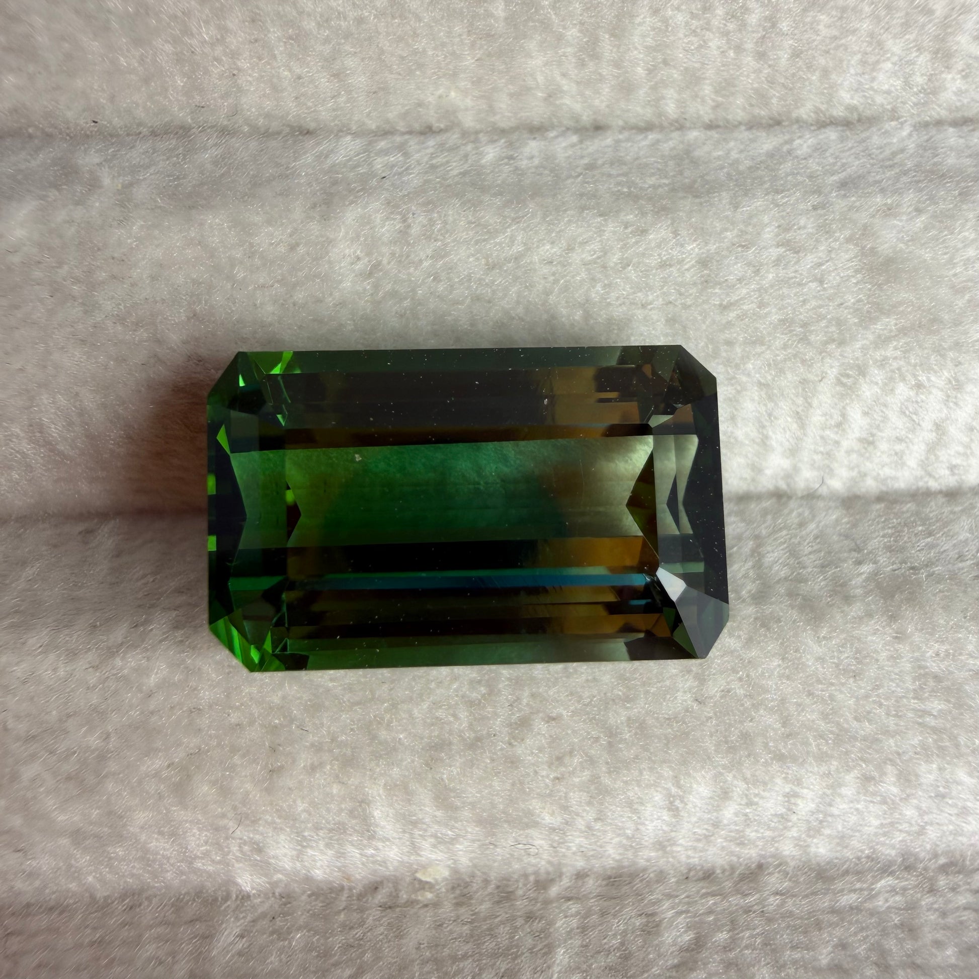 Rectangular green gemstone on a gray fabric background