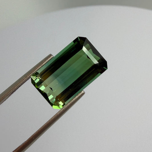 Green gemstone held by tweezers on a neutral background