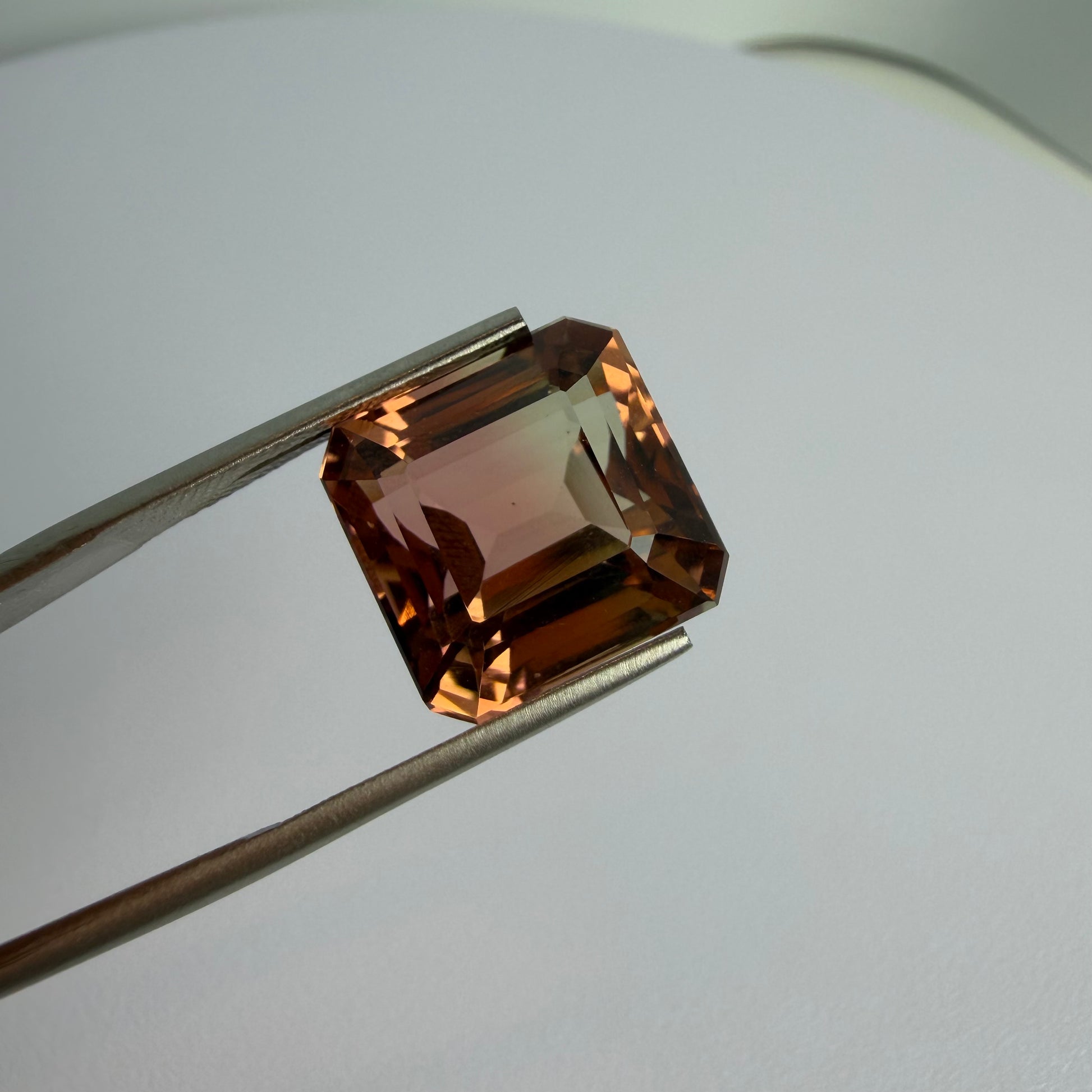 Brown gemstone held by tweezers on a light gray background