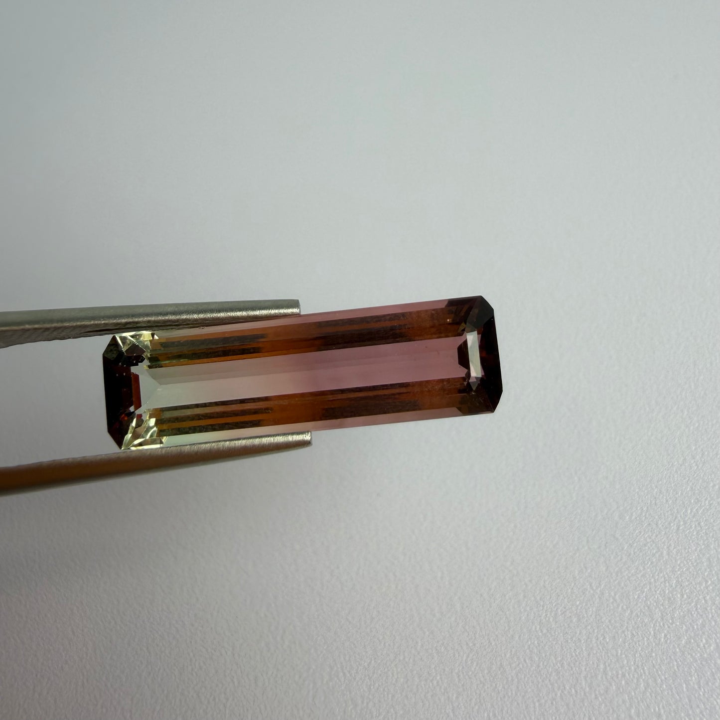 Brown rectangular gemstone held by tweezers on a light gray background