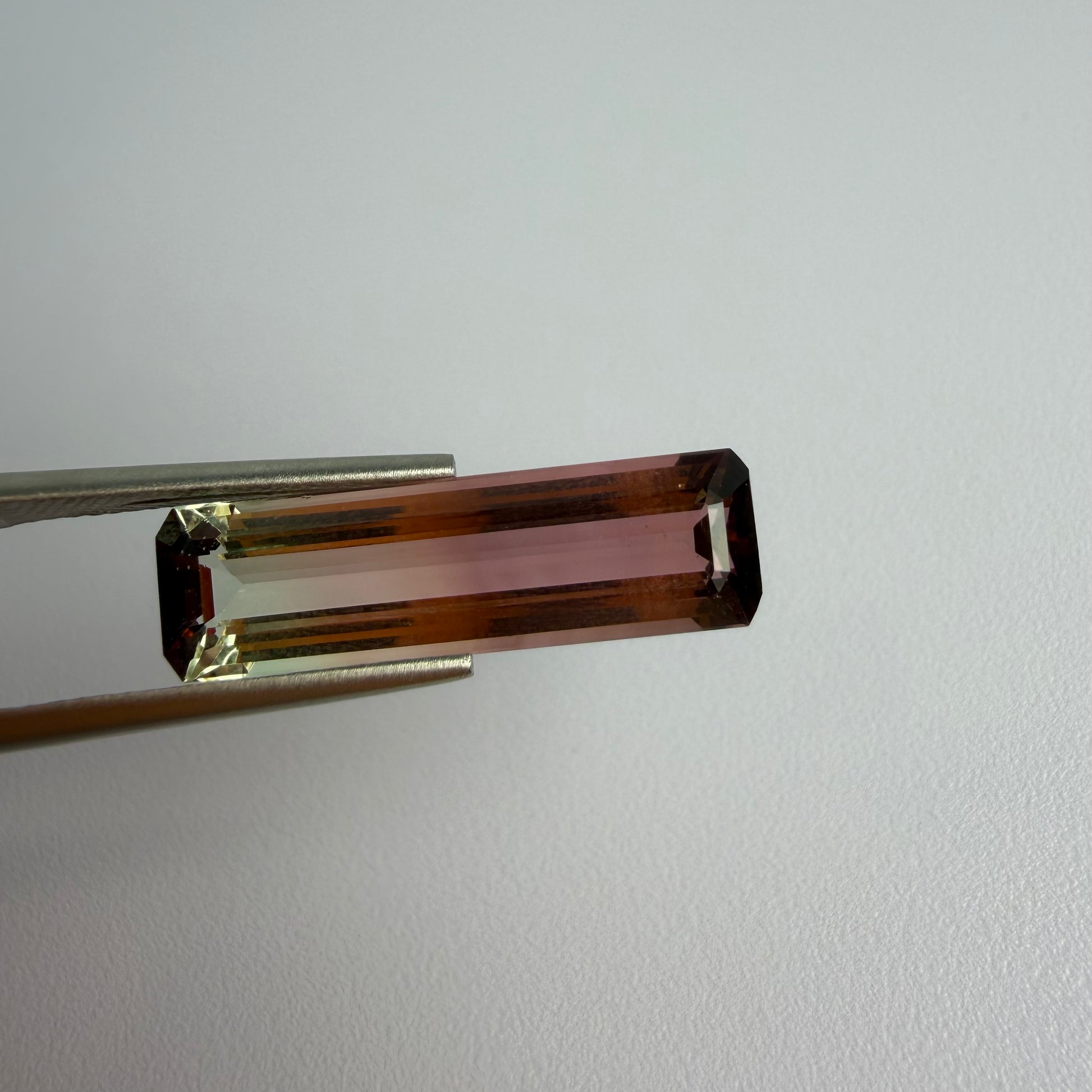 Brown rectangular gemstone held by tweezers on a light gray background