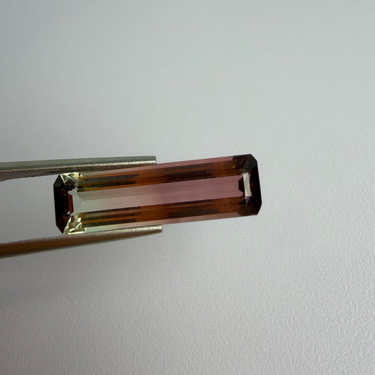 Brown rectangular gemstone held by tweezers on a light gray background