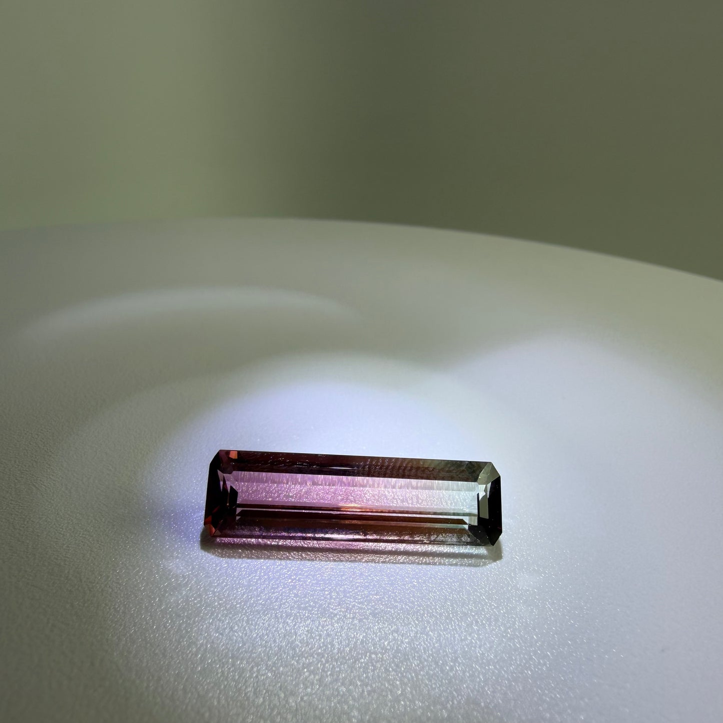 Rectangular purple gemstone on a reflective surface with a neutral background