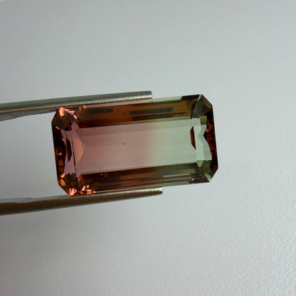 Rectangular gemstone held by tweezers on a light gray background