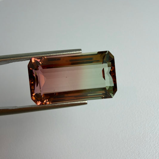 Rectangular gemstone held by tweezers on a light gray background