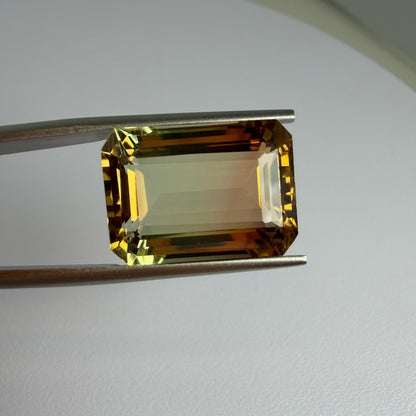 Faceted yellow gemstone held by tweezers on a light gray background